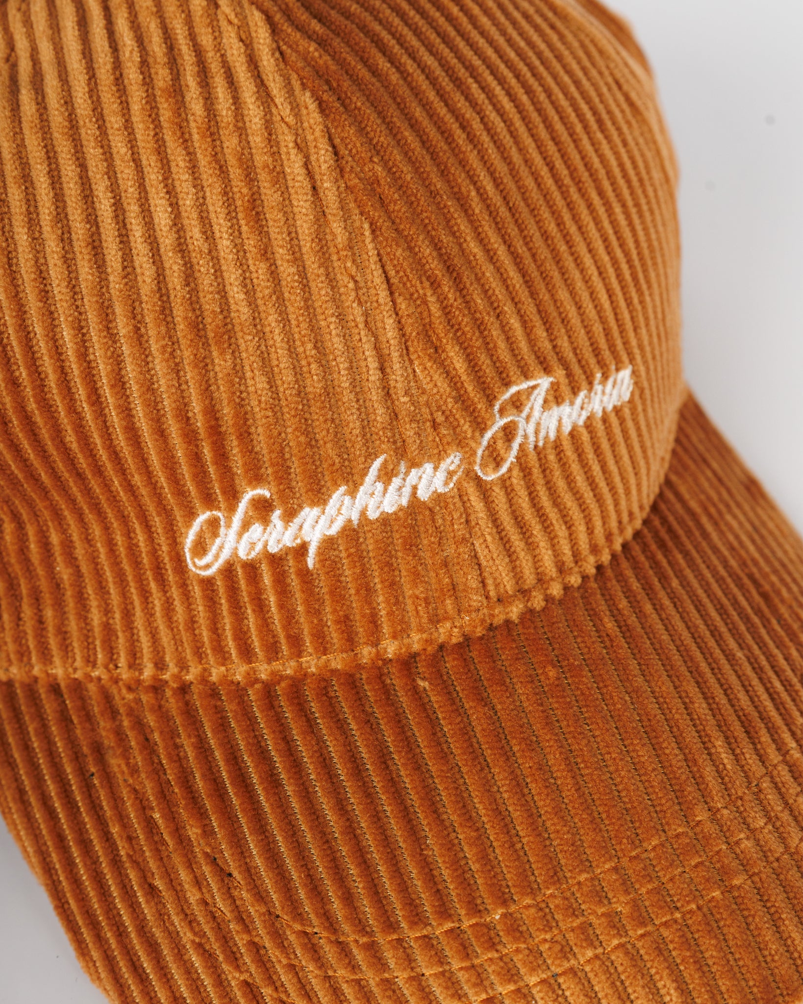 Brown corduroy cap with white embroidered text on a white background